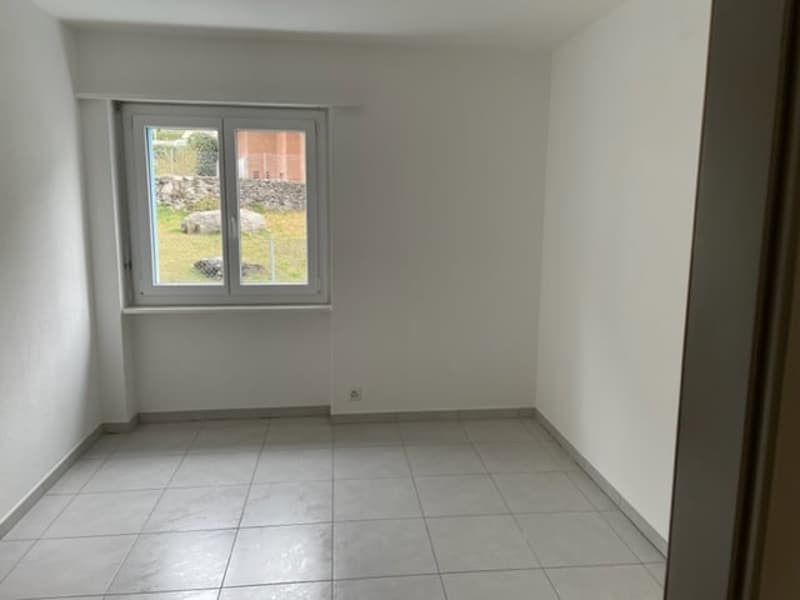 Spacious room with white walls, tiled floor, and a large window overlooking the outdoor area.