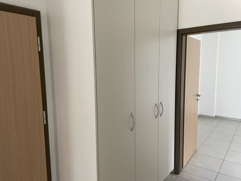 The image shows a room with white walls, a wooden door, and a built-in wardrobe with gray doors. The floor appears to be tiled.