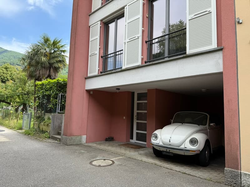 2-story residential building with a red exterior, white windows, and shutters. A classic Volkswagen Beetle is parked in the garage underneath the building.