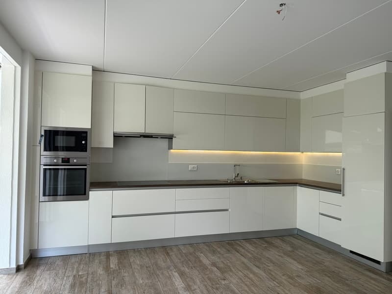 Modern, L-shaped kitchen with white cabinets, built-in oven and microwave, and a wooden countertop. The kitchen has LED lighting under the cabinets and a hardwood floor.