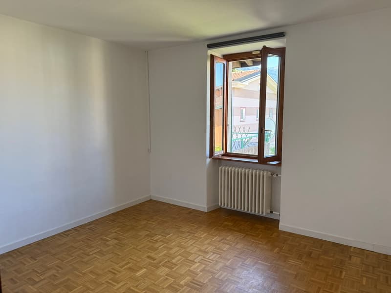 Spacious bedroom with hardwood parquet flooring, white walls, and a large window providing natural light. The room appears to be empty, ready for furnishing and personalization.