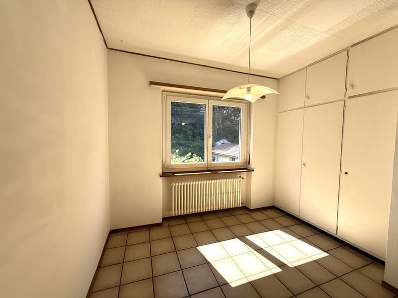 Spacious room with tile flooring, white walls, large windows overlooking a garden, and a pendant light fixture.