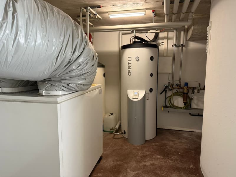 Utility room with white and gray water tanks, electrical outlets, and pipes.