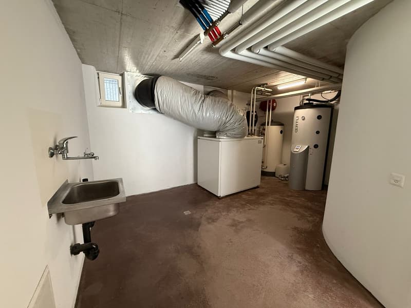 Small, clean, white room with a sink, water pipes and a washing machine.