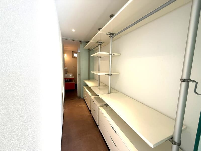 modern wardrobe with white shelves and metal rods, several white drawers, brown tiled floor, glass door