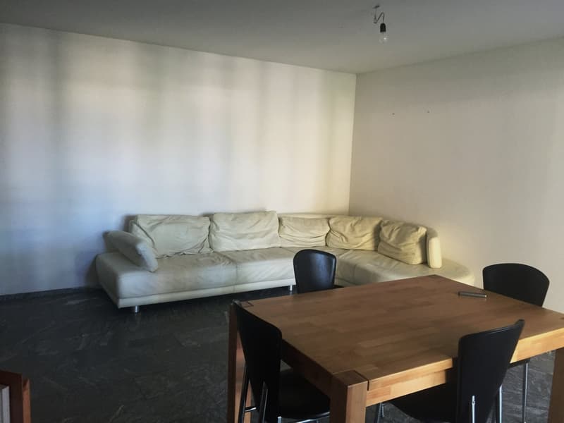 Large white sofa, wooden dining table with 4 black chairs, light brown table top, floor lamp on the wall