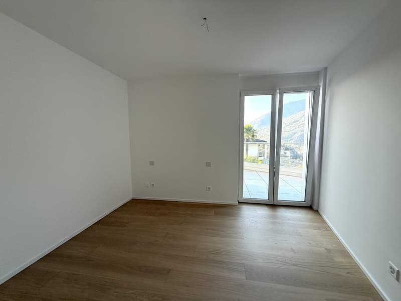 Empty room with sliding glass doors leading to a terrace, wooden floor, white walls, no furniture, and a scenic view of a mountain range.