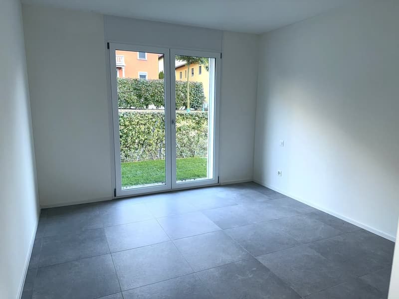 Empty room, tiled floor, glass sliding door, white walls, garden view outside