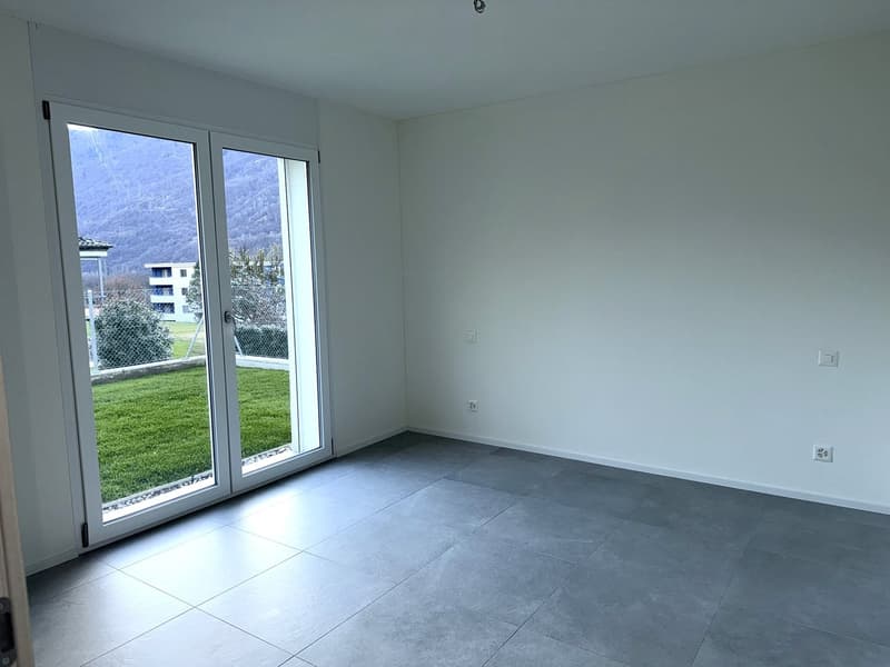 Empty room with gray tiled floor, large sliding glass doors leading to a grassy area, large windows, white walls
