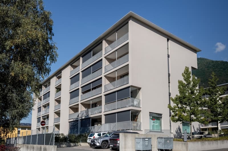 Modern apartment building, grey walls, multiple balconies, ground floor commercial space