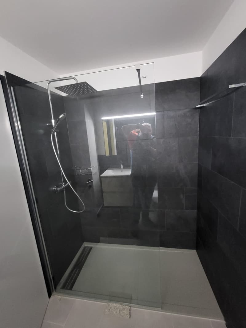 Modern walk-in shower, shower head and hose, illuminated mirror, tiled floor, tiled walls, sink, toilet