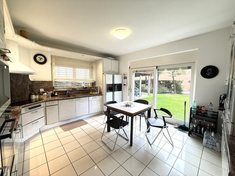 modern kitchen with white cabinets, black countertops, white tiled floor, dining table, chairs, sliding glass door, garden view