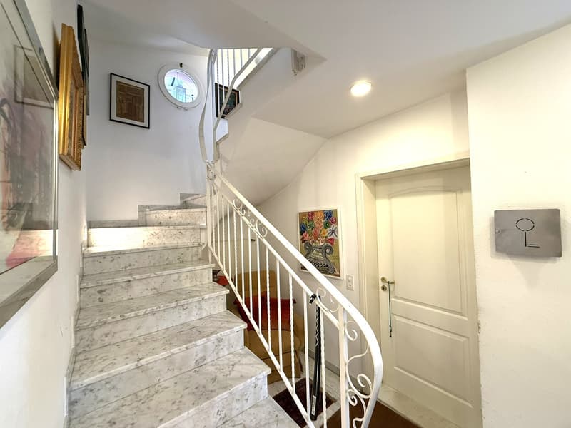 marble stairs with railing, arched window, framed artworks, closed door, key holder