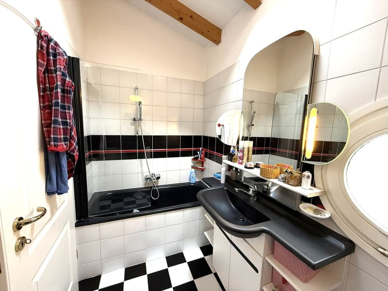 Bathroom with black and white checkered tiles, bathtub, sink, mirror, and wooden ceiling beams.
