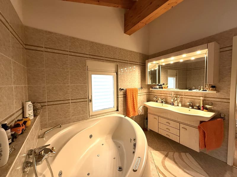 modern bathroom with a bathtub, double sink, mirror, wooden cabinets, wooden beams, tiled walls, window
