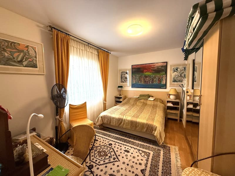 large bed, bedspread, two nightstands, lamp, nightstand, armchair, carpet, fan, rug, chairs, wooden floor, curtains, window, paintings