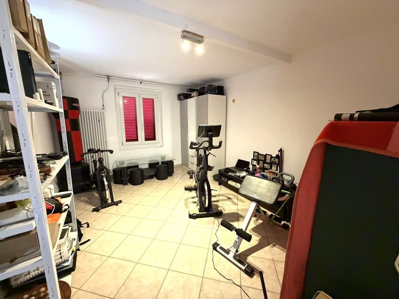 A room with exercise equipment, a white cabinet, a radiator, and a window with red shutters