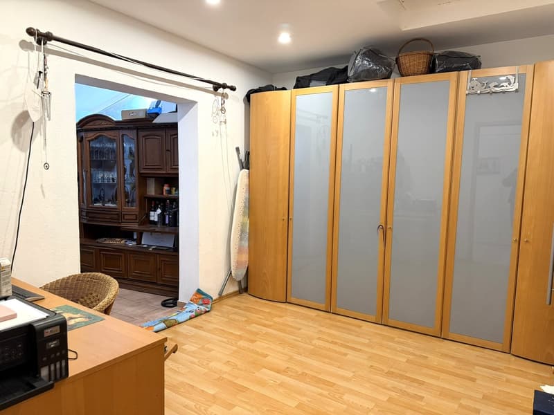 wooden floor, wooden wardrobe, wooden desk, basket on top of wardrobe, cabinet with wine glasses, ironing board