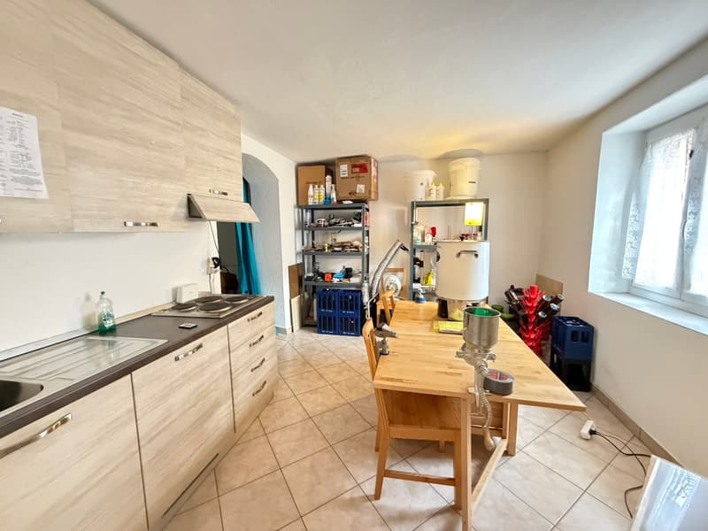 kitchen with wooden cabinets, tiled floor, wooden dining table, shelves with various items, window with white curtains