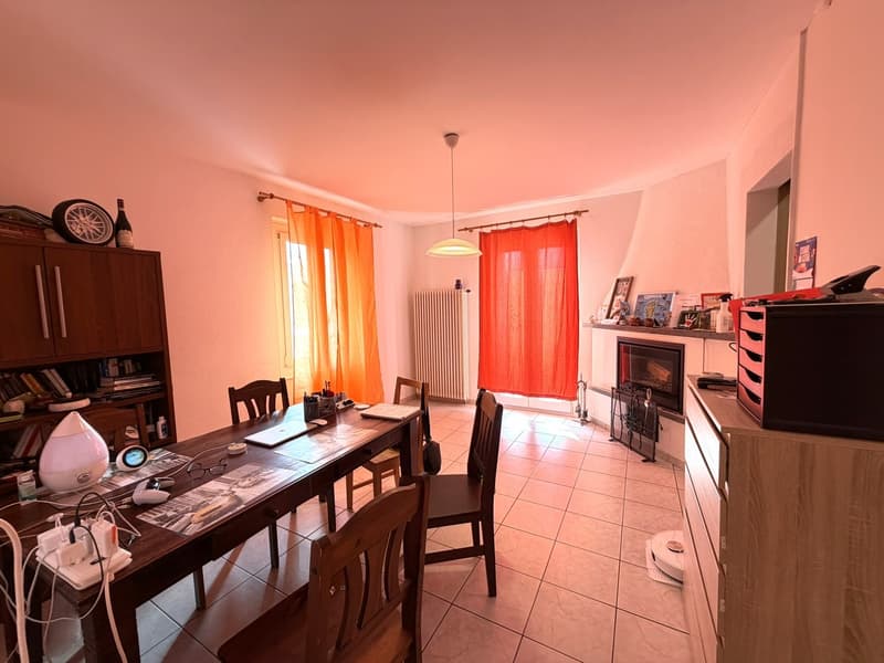 Dining room with wooden table, chairs, fireplace, radiator, bookshelves, and various items on the table
