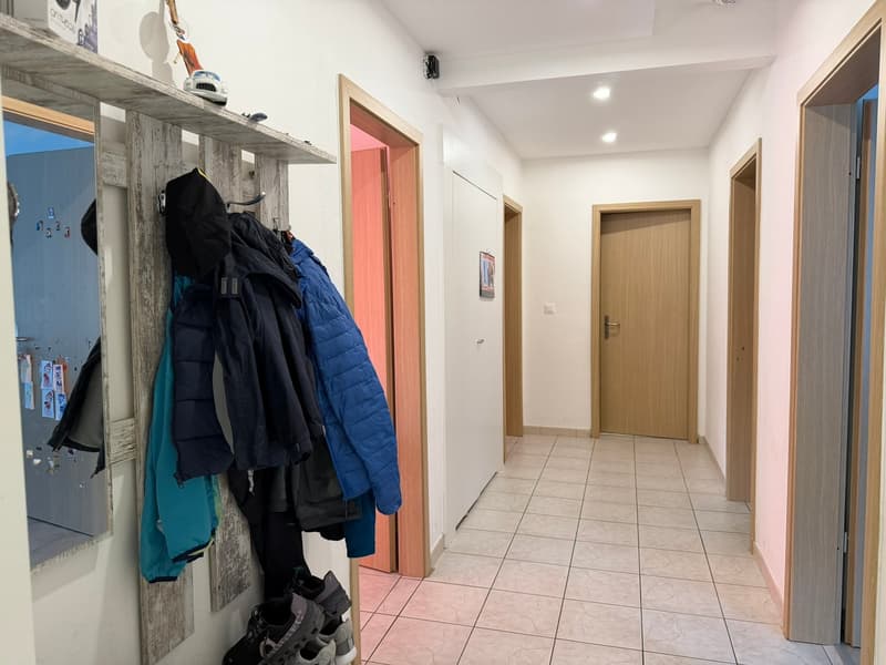A hallway with tiled floor, wooden doors, a wooden coat rack with jackets and shoes, a mirror, and a picture frame on the wall.