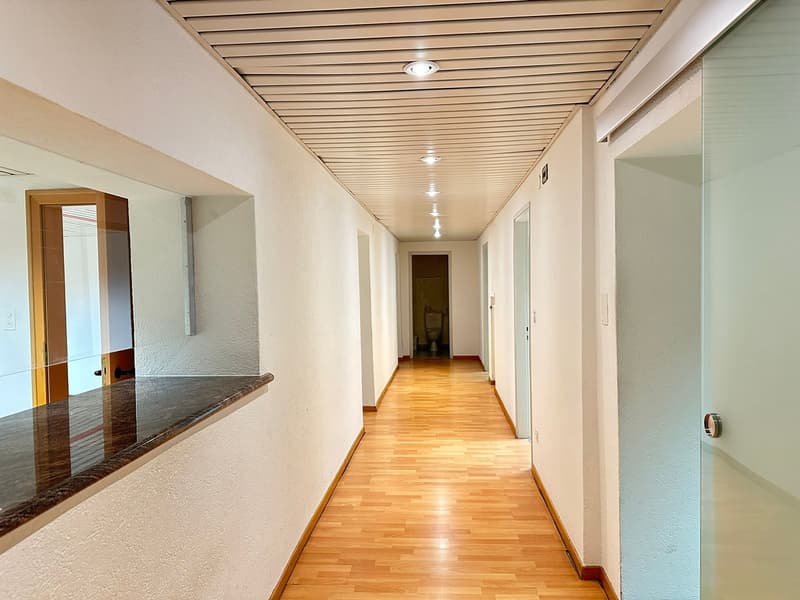 Empty hallway with wooden floor, white walls, glass doors, and a marble countertop.