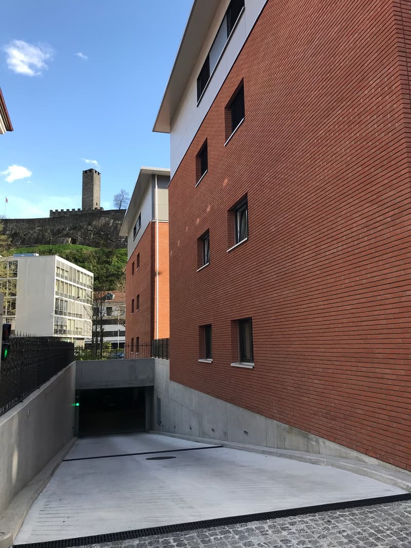 Red brick building, multiple windows, concrete parking area, metal fence, underground garage