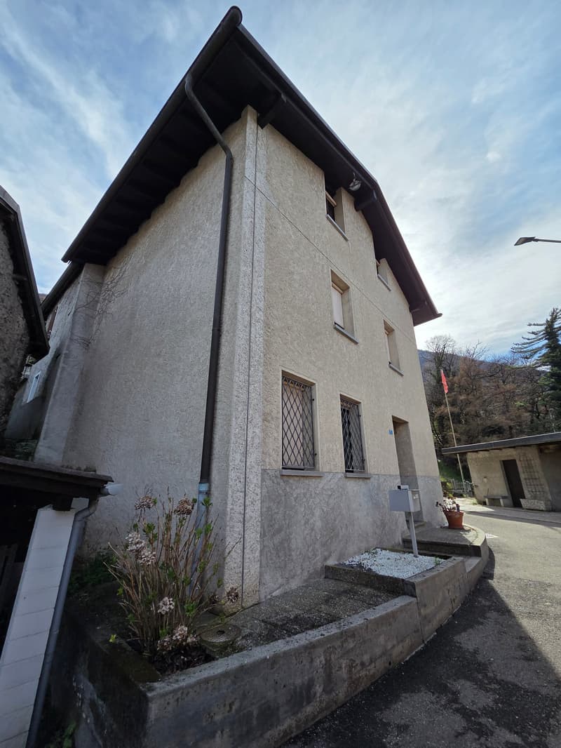 2 story house, concrete wall, windows with metal grills, chimney, plants in front