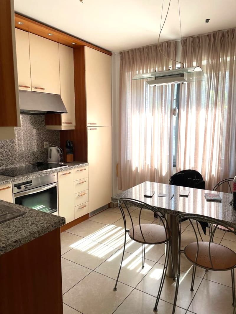 modern kitchen with granite countertops, stainless steel appliances, wooden cabinets, tiled floor, dining table with chairs, large window with curtains