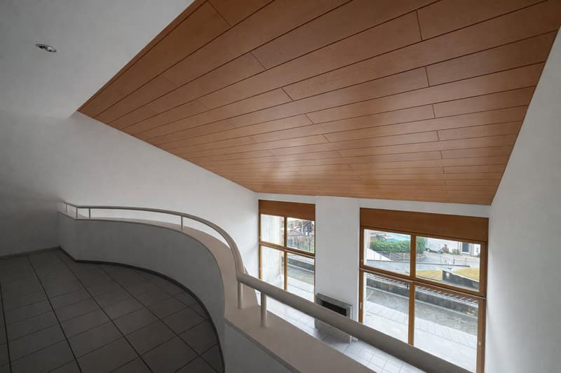 Curved balcony with tiled floor, white walls, wooden ceiling, two large windows, fireplace