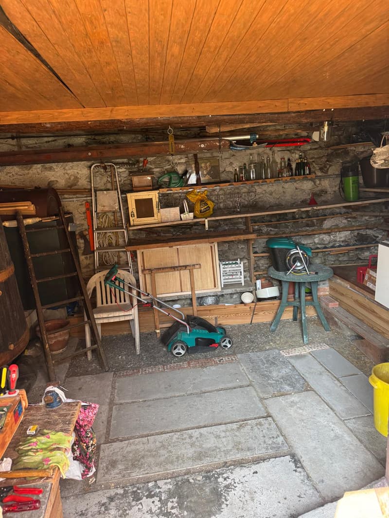 A storage room with wooden ceiling, shelves, ladder, table, chair, and various items