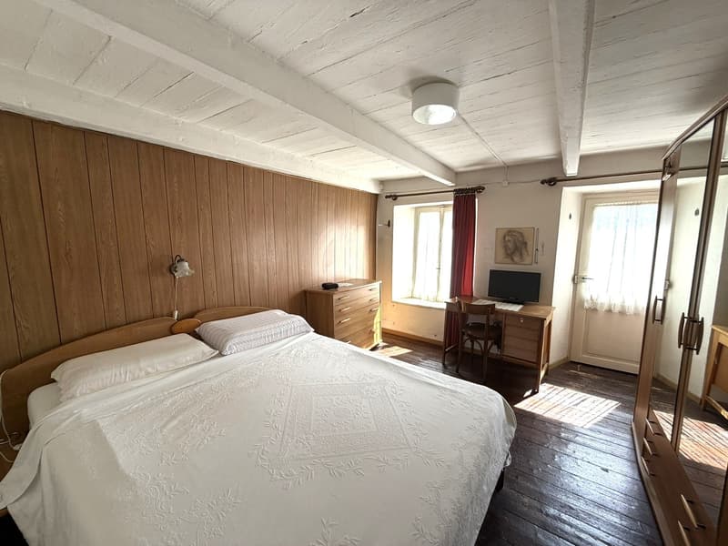Bedroom with wooden walls, bed, desk, chair, monitor, wooden cabinet, lamp, picture frame, wooden floor, wooden door, and window with curtains
