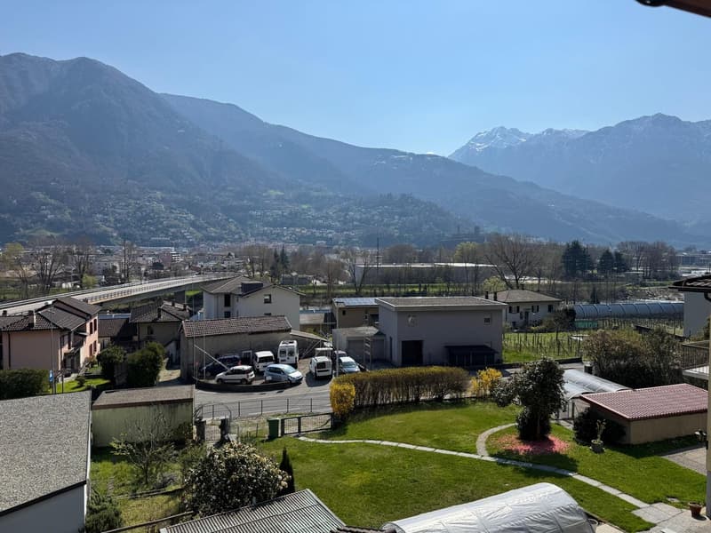 Aerial view of a residential area with several houses, a parking lot, and a bridge in the distance. Mountains and a city in the background.