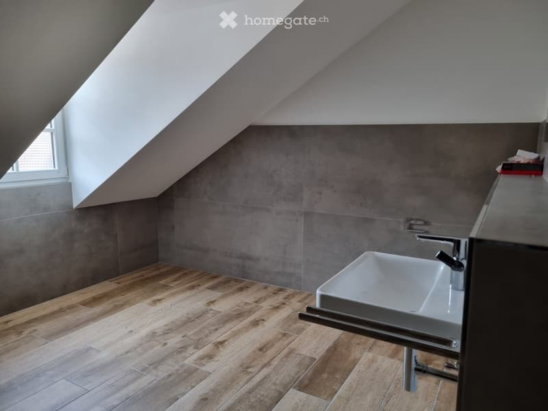 white sink, grey tiles on wall, wooden tiles on floor, white walls, metal faucet, window on ceiling