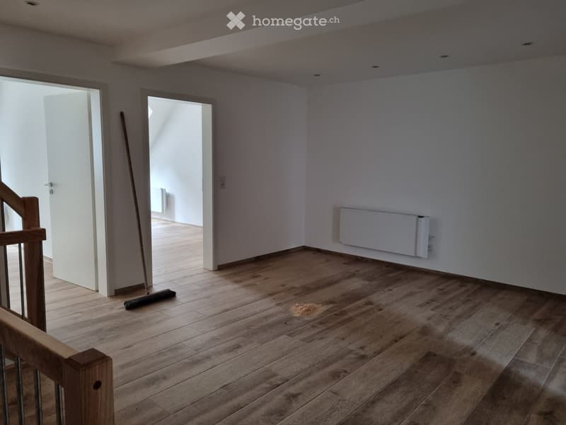 Wooden floor, white walls, empty space, radiator on wall, broom and dustpan, wooden staircase