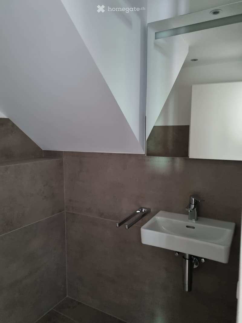 gray tiled walls, white sink, chrome faucet, mirror mounted on wall, sloped ceiling