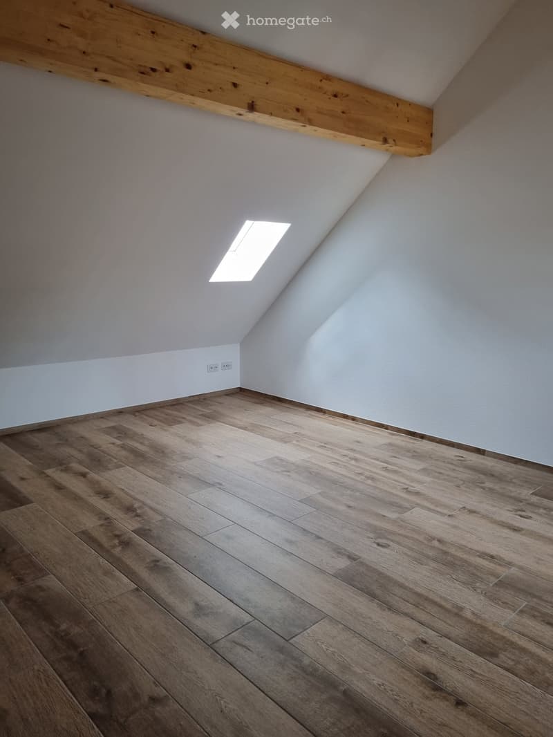 empty room with wooden floors, white walls, and a wooden beam on ceiling. An attic window provides natural light.