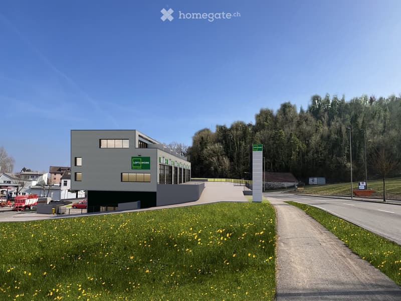 Modern two-story building with a grey exterior, windows, and green signage, situated on a sloped landscape with a pathway leading to the entrance.