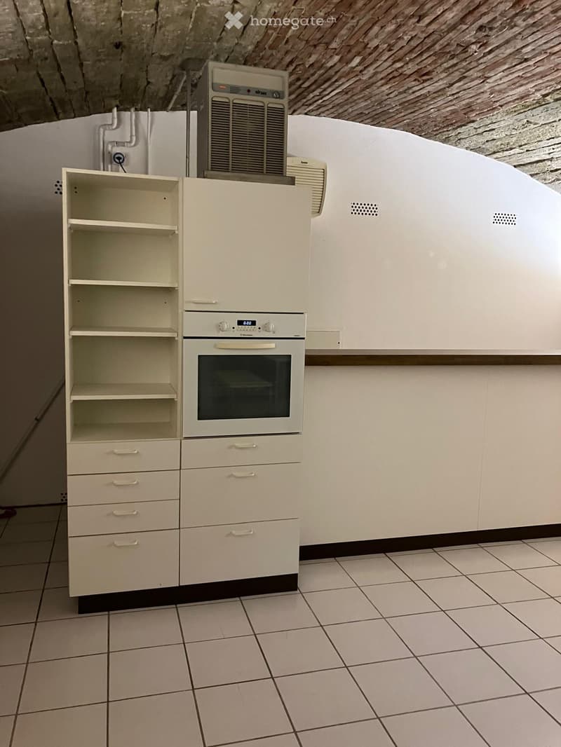 Empty kitchen with white tiles, white cabinets, shelf, and built-in oven, with visible wiring on the wall.