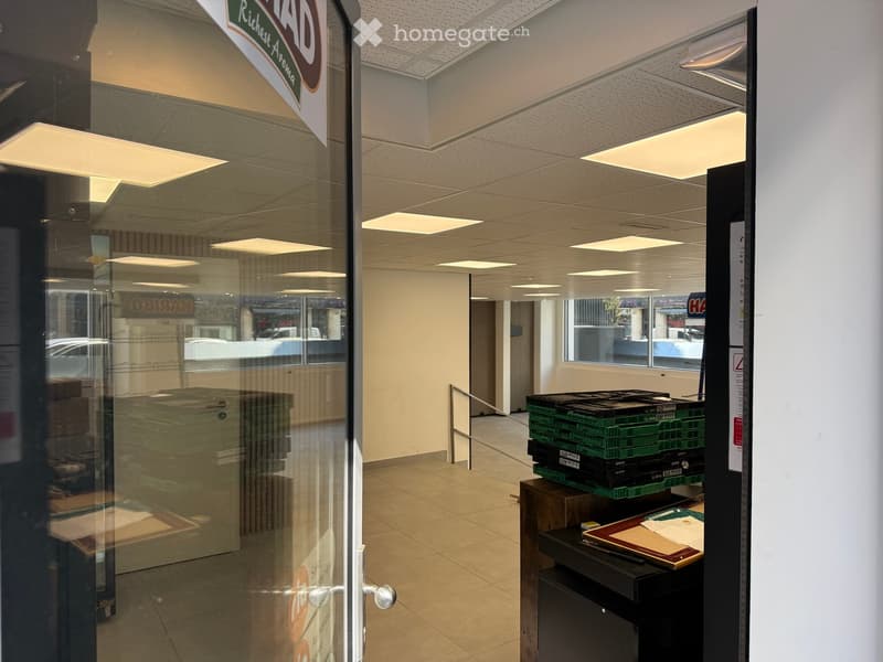 Empty room with tiled floor, glass door, white walls, ceiling with recessed lighting, storage boxes, and a handrail.