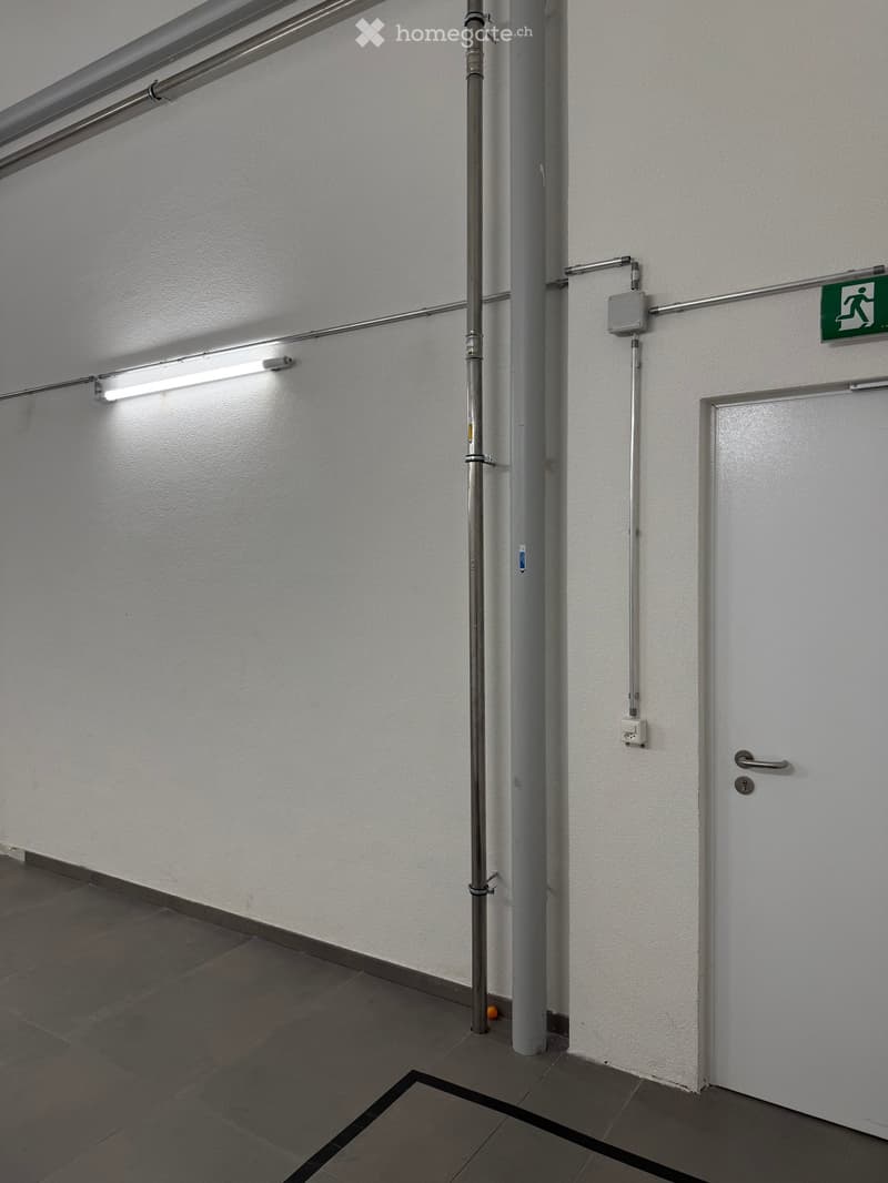 white walls, gray tile floor, a door, pipes and electrical outlets mounted on the wall