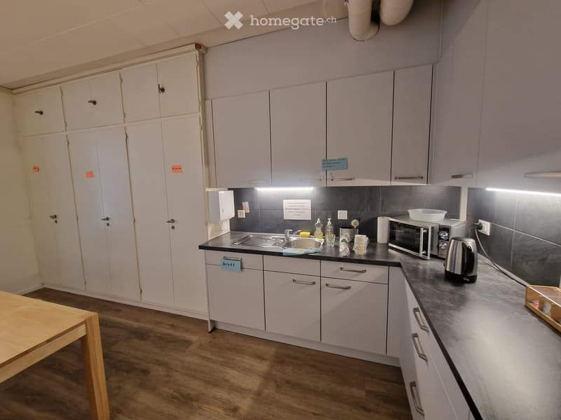 Kitchen with wooden floor, white cabinets, countertop, sink, cabinets, microwave, tea kettle, and countertop lighting.