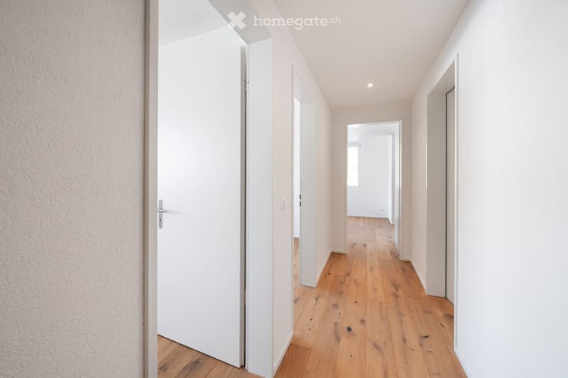 Empty corridor with white walls, wooden floor, and closed doors on both sides.