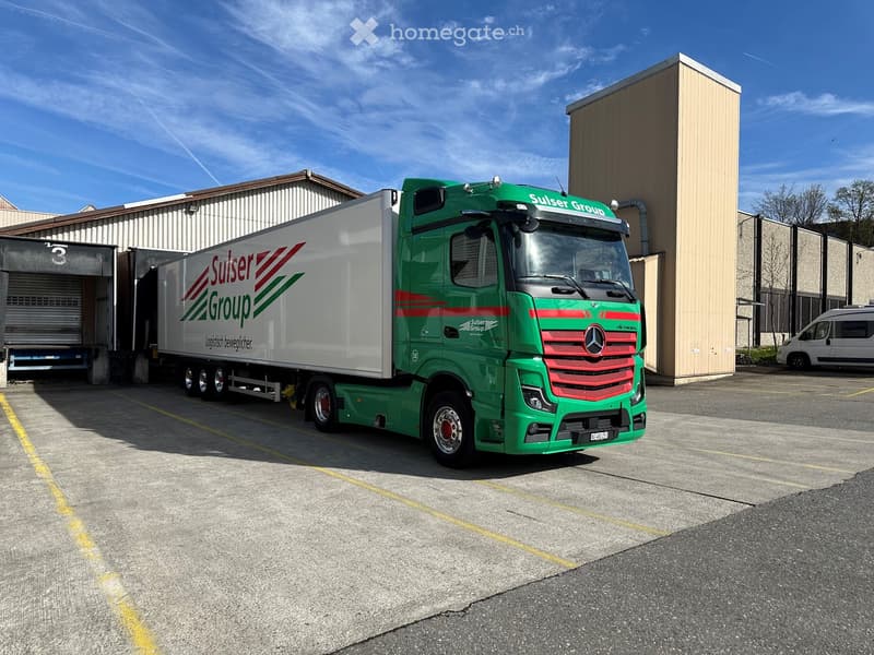 Large green Mercedes semi-truck parked outside warehouse, brand name reads Sulser Group.