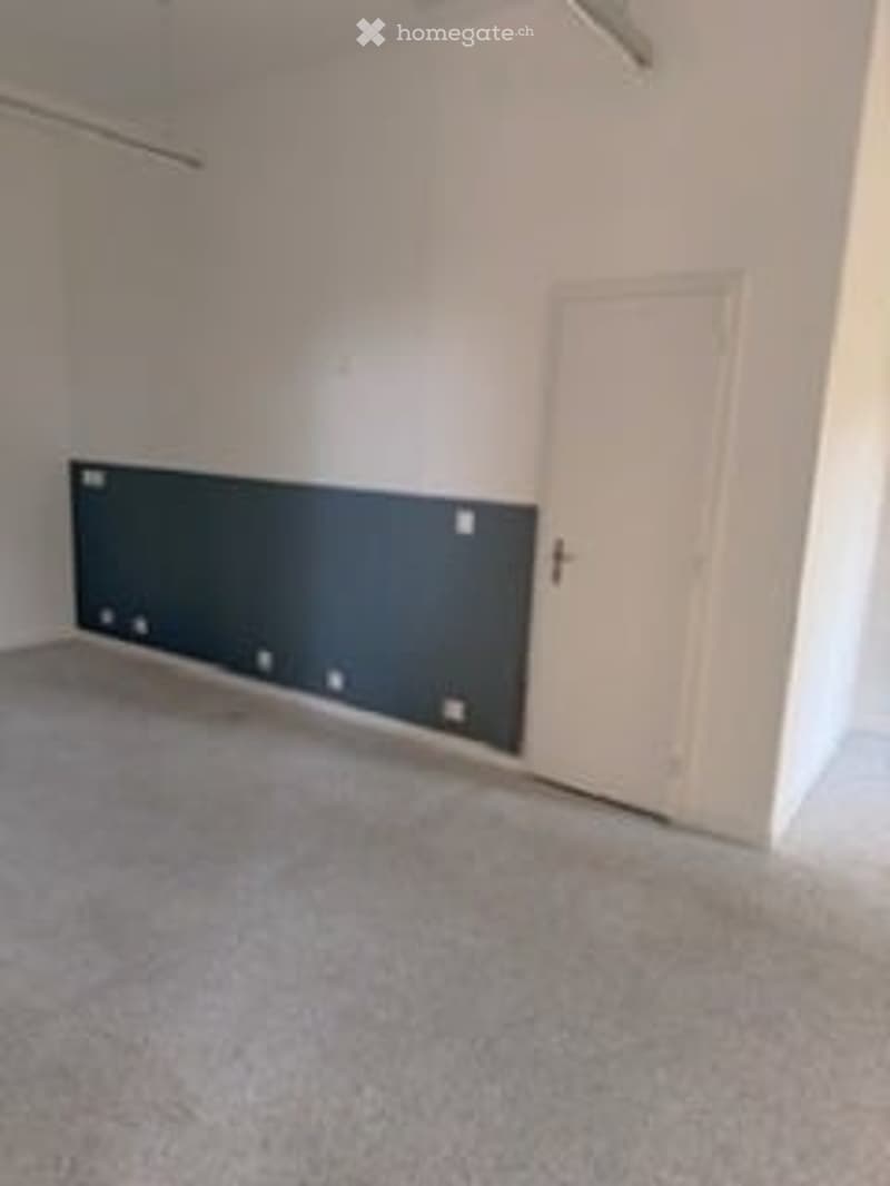 Empty room with white walls, grey carpet, one white door, black accent wall with power outlets, empty