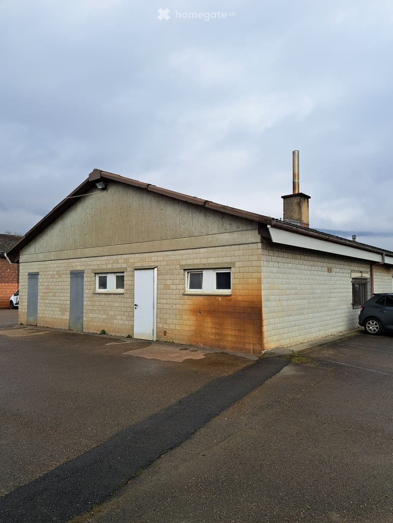 A single story commercial building, brick walls, white doors, two windows, a chimney, parking space in front.
