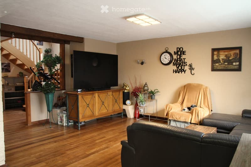 wooden floor, mounted TV, covered chair, black sofa, coffee table, clock on wall