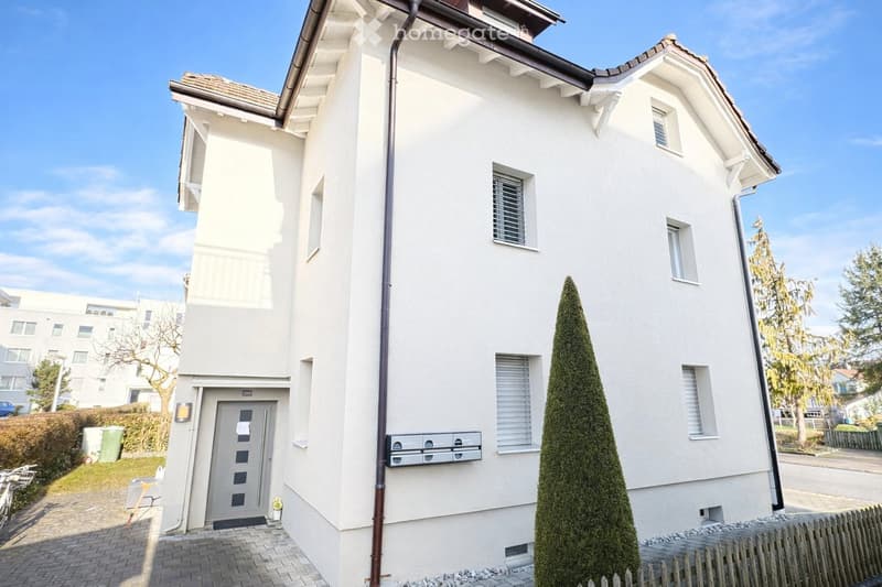 2 story house, white exterior, brown roof, multiple windows, entrance door, small garden, bicycles