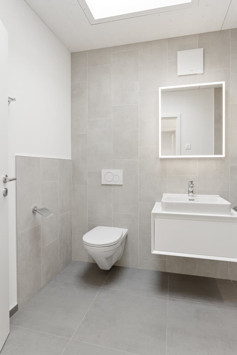 Modern bathroom with white tiles, a toilet, a sink, a mirror, and a soap dispenser.