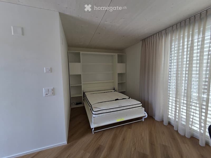 A room with a bed, shelves, and a window with curtains.